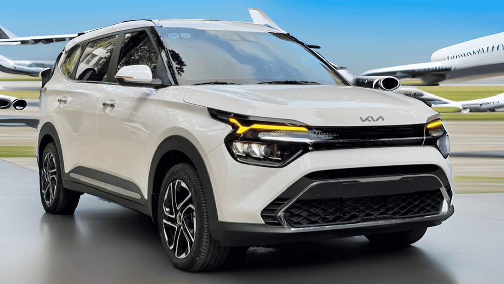 A white Kia SUV with distinctive headlights and a front grille, parked on a tarmac with an airplane in the background. 2