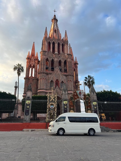 A historic cathedral with intricate Gothic architecture, a white van parked in front, and a red wall. 1