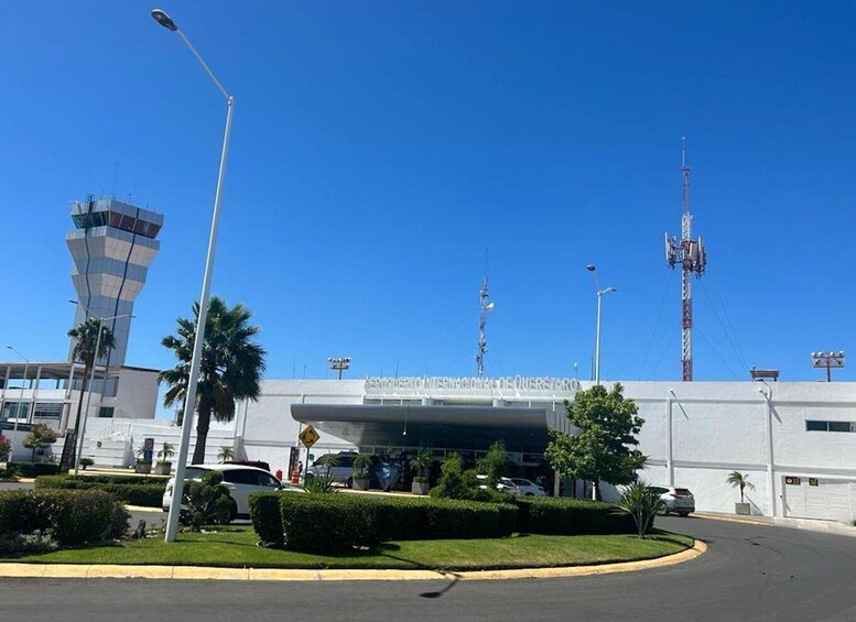 An airport terminal with a clear blue sky, palm trees, and a control tower. 3