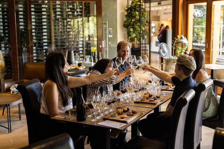 A group of people toasting with wine glasses at a restaurant with a long table and wine bottles. 2