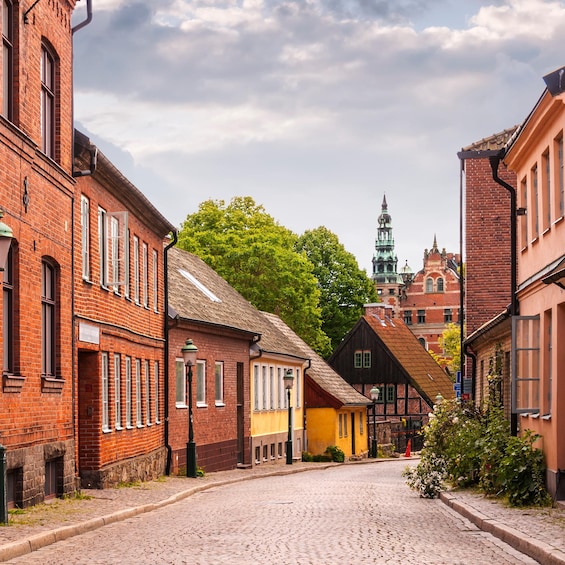 A cobblestone street lined with historic buildings, including a church with a spire and a traditional half-timbered house. 2