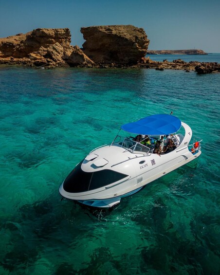 A white boat with a blue canopy and the word "ESCAPE" on its side, floating on clear turquoise water with rocky formations in the background. 5