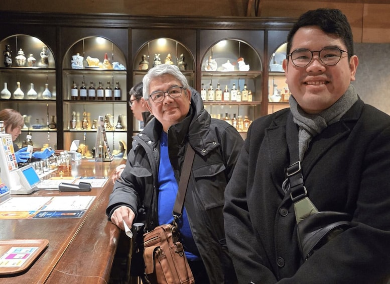Two people at a bar with shelves of bottles in the background. 2