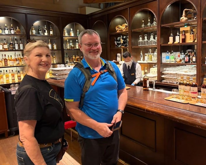 A man and a woman standing in a bar with shelves of bottles and glasses. 3