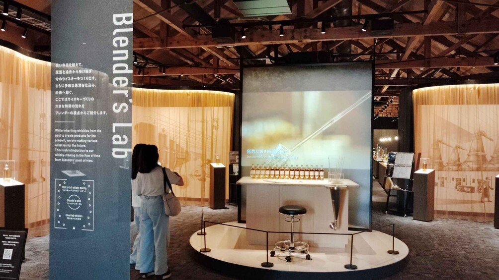 A museum exhibit with a central display of whisky bottles, surrounded by informational panels and a person observing. 2