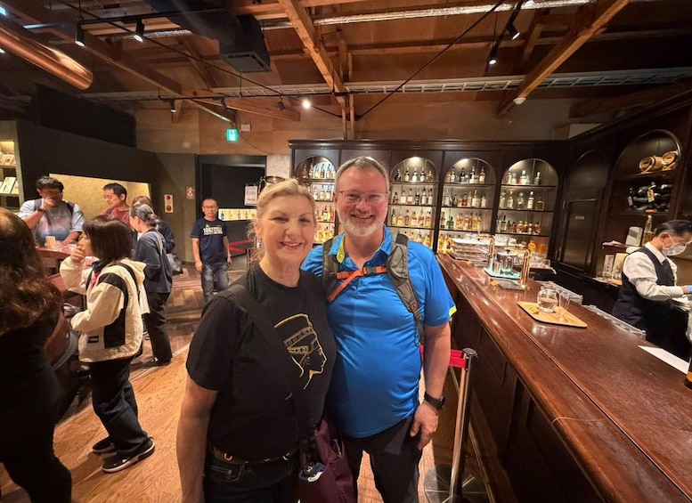 A bar with wooden beams, shelves of bottles, and a person in a blue shirt standing at the counter. 2
