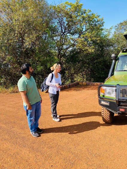 Two people standing on a dirt path with a green vehicle parked nearby. 4