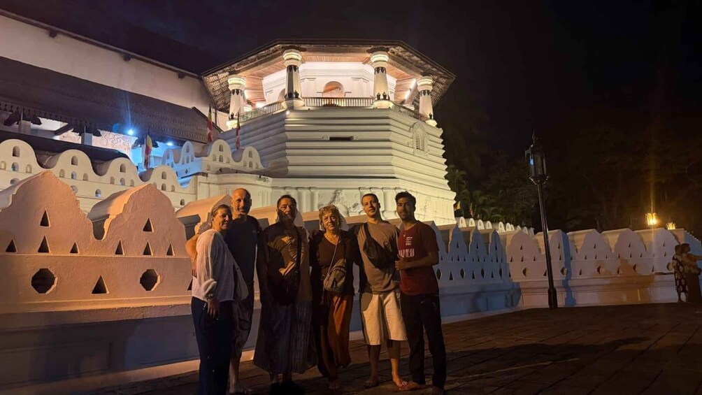 A group of people standing in front of a large, illuminated building with a white facade and a series of arches. 4