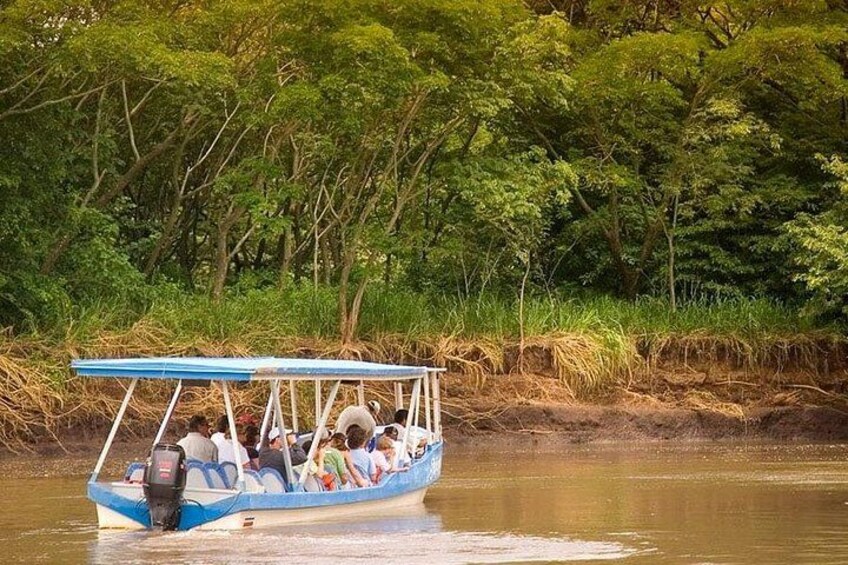 A blue boat with passengers on a calm river surrounded by dense greenery. 1