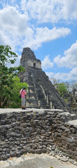 A person taking a photo of a large ancient stone structure with a clear blue sky in the background. 3