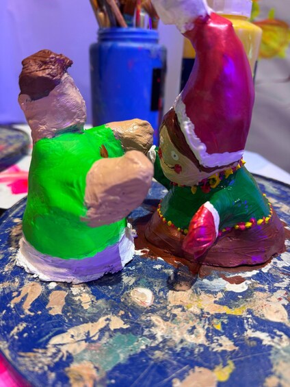 A sculpture of a man and a woman in colorful paint, with a blue can and paintbrushes in the background. 4