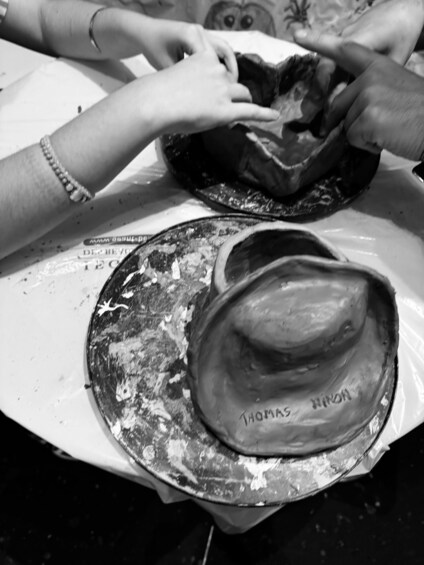 A person shaping a clay hat on a table. 5