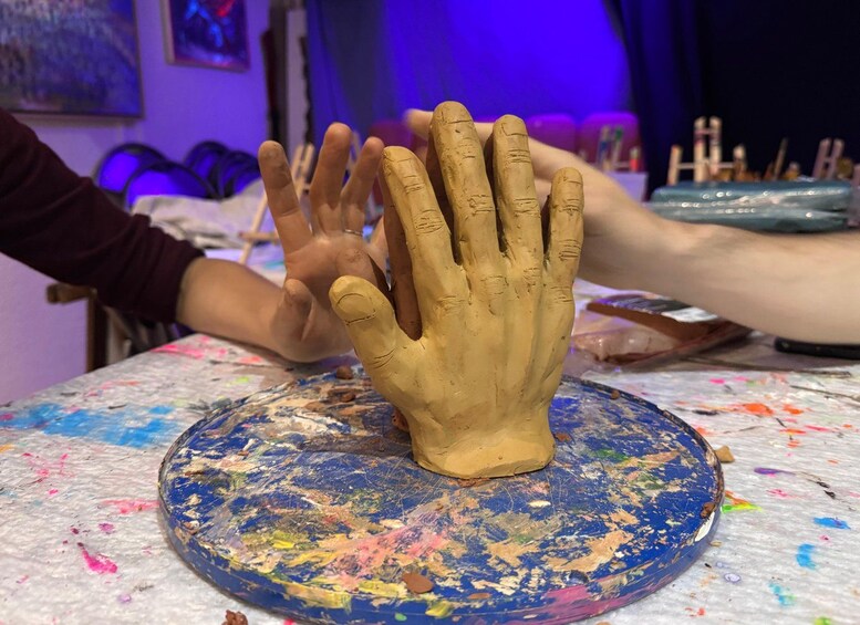 A hand sculpture on a paint-splattered table with paintbrushes and jars in the background. 1
