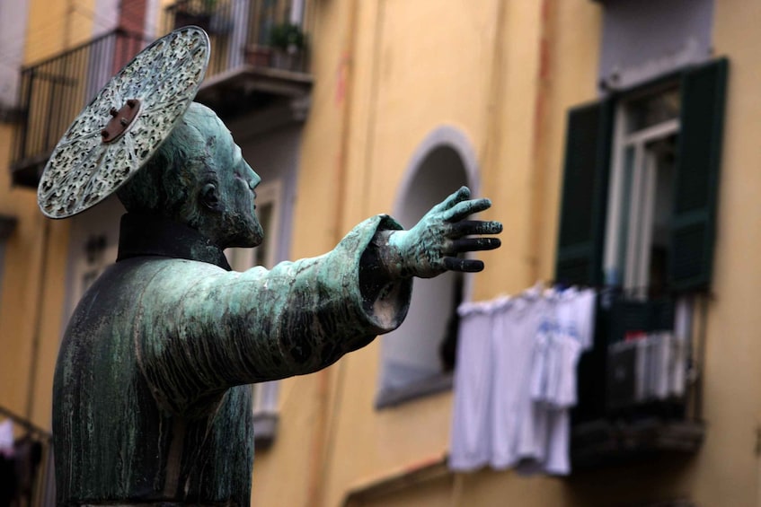 A bronze statue of a figure with a hat and outstretched arms. 2