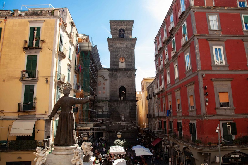 A bustling street with a prominent clock tower, a statue, and colorful buildings. 5