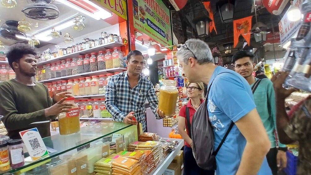 A busy market with people shopping and a man holding a large jar. 1