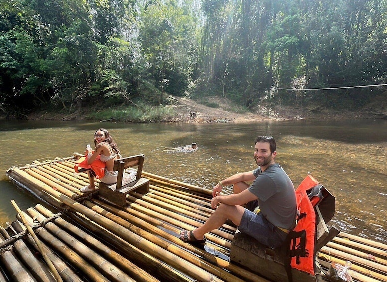 Two people on a bamboo raft in a river surrounded by dense forest. 3