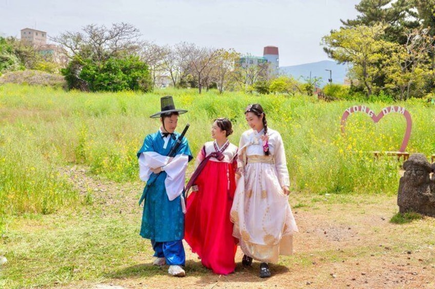 Three people in traditional attire standing in a field with a sign that reads 'Yongdam.' 1