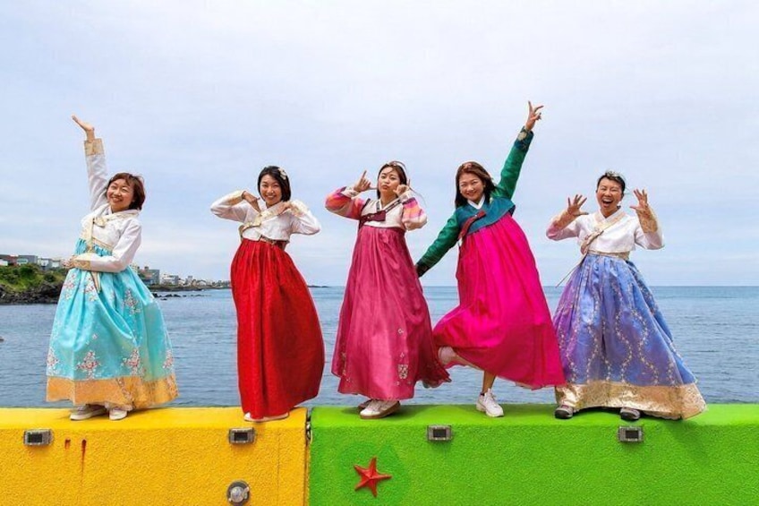 A group of people in traditional attire on a stage by the water. 4