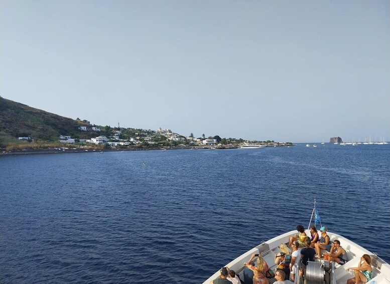 A boat with people on a calm sea, a coastal town in the background, and a rocky outcrop in the distance. 2