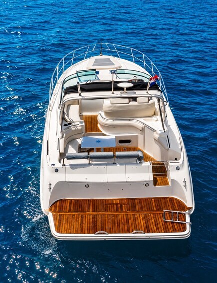 A white motorboat with a wooden deck and seating area, floating on blue water. 2