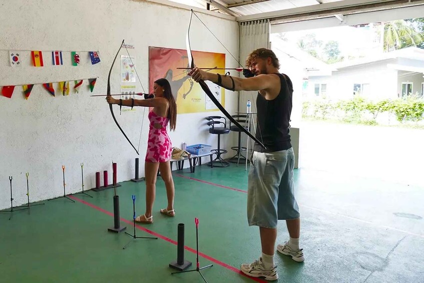 Two people practicing archery indoors with targets and flags on the wall. 4