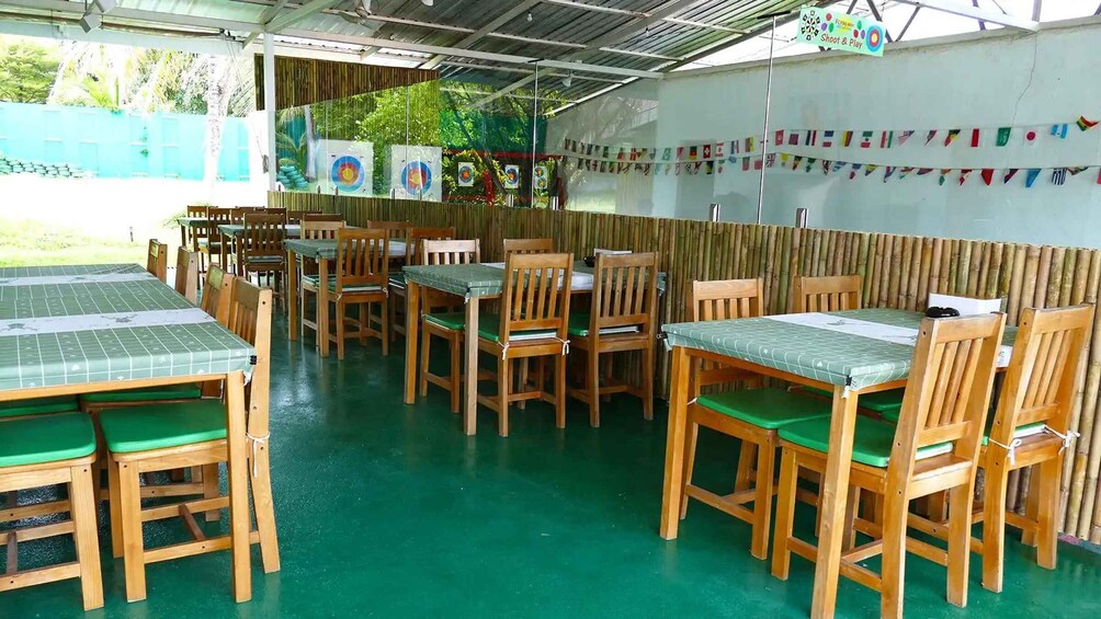 A covered outdoor dining area with wooden tables and chairs, a green floor, and a wall decorated with flags. 2