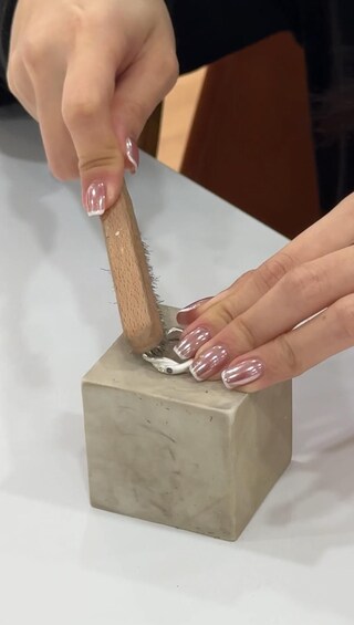 A person using a wooden-handled tool on a small, rectangular, light-colored block. 5