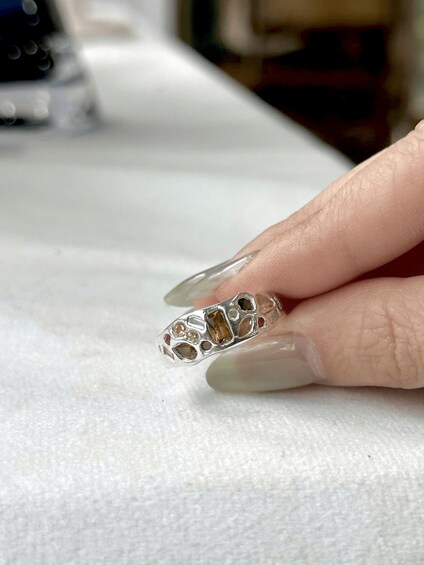 A hand holding a silver ring with a large central gemstone and smaller stones. 2