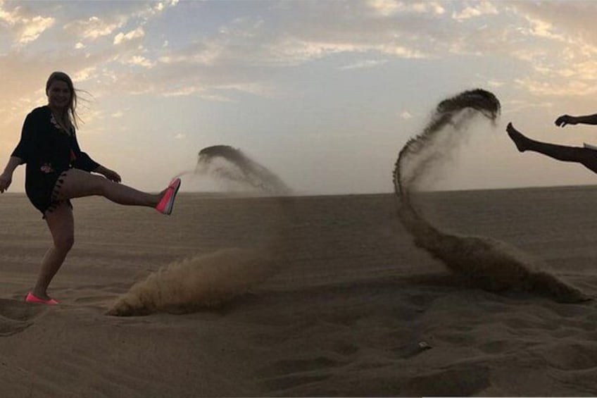 A person kicking up sand on a beach with a large wave in the background. 3