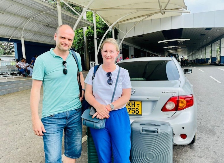 Two people standing in front of a car with a license plate. 1