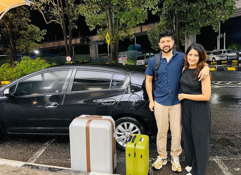 A black car parked in a wet parking lot with two suitcases in front. 4