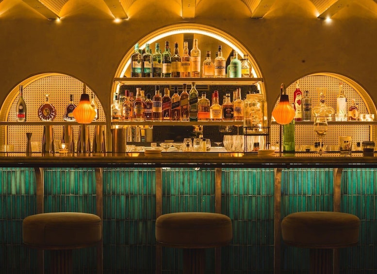 A bar with a variety of liquor bottles and glasses, and three stools in the foreground. 2