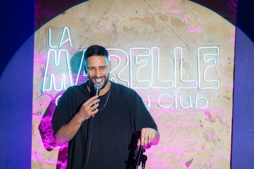 A person holding a microphone in front of a neon sign that reads 'LA MARELLE CLUB'. 3