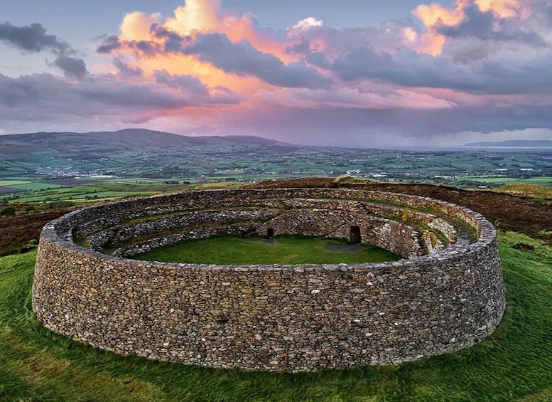 A stone ring structure with a grassy center, surrounded by rolling hills and a cloudy sky. 1