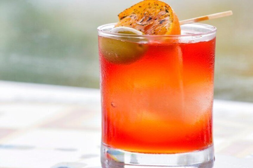 Un vaso alto con una bebida roja, una rodaja de fruta y una pajita. 1