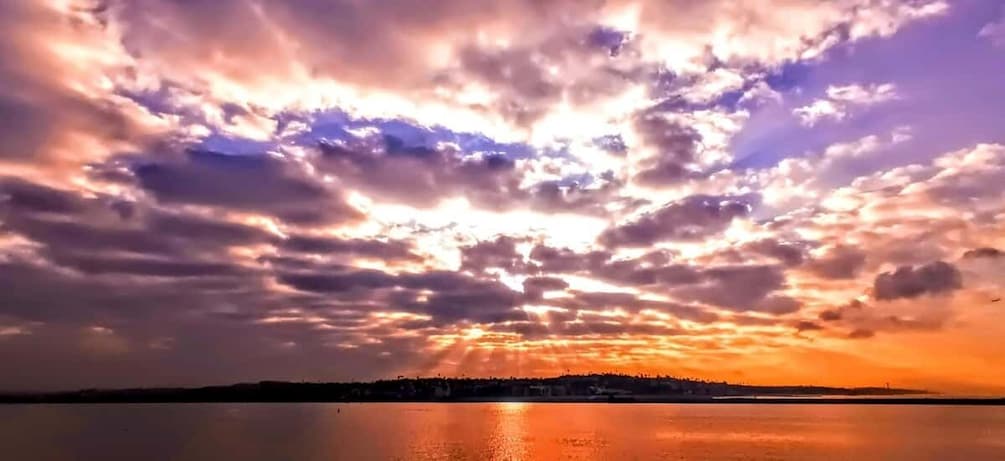 Auringonlasku vesistön yllä, ja kauempana näkyvän maa-alueen hahmo piirtyy siluetin muodossa taivaalle. 5