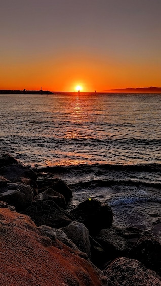Auringonlasku tyynen meren yllä, etualalla näkyy kallioita. 4
