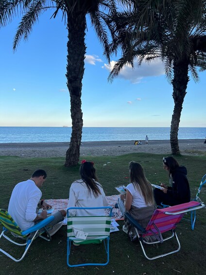 Four people sitting on colorful chairs under palm trees by the beach. 2