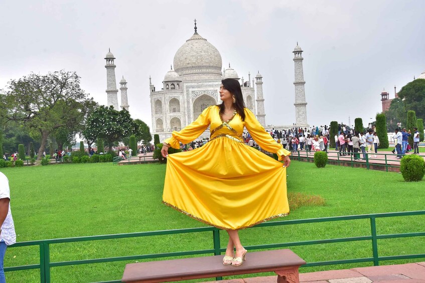 A person in a yellow dress standing on a bench with the Taj Mahal in the background. 2