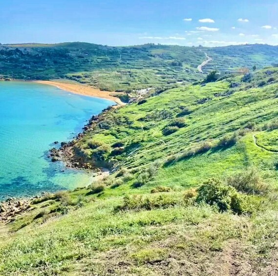 A coastal landscape with a clear blue sea, green hills, and a winding road. 4
