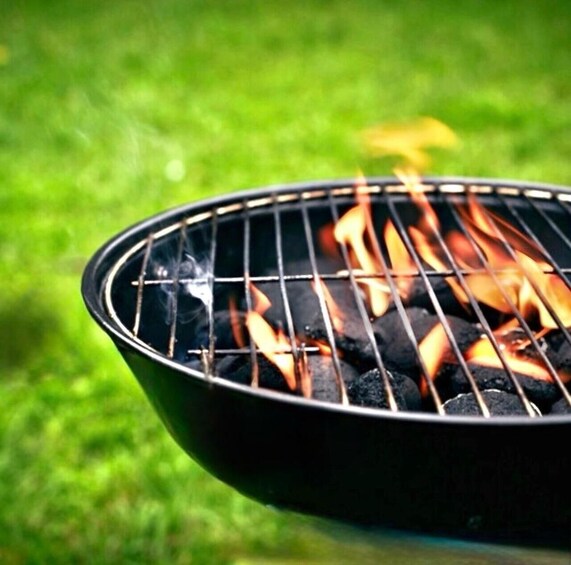 A grill with flames burning charcoal on a grassy surface. 1