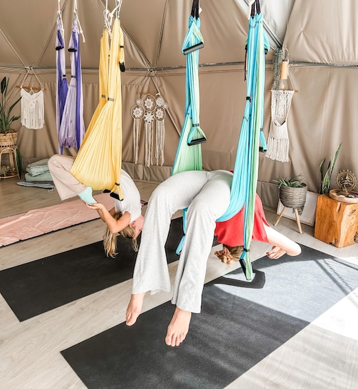Two people performing aerial yoga in a tent with colorful hammocks. 4