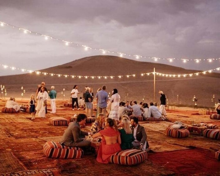 A group of people sitting on cushions in an outdoor setting with string lights overhead. 1