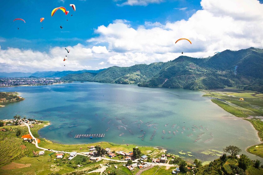 A lake surrounded by hills, with several paragliders in the sky. 2