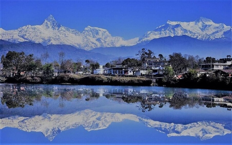 A lake with a mountain range in the background and a small settlement with houses along the shore. 1