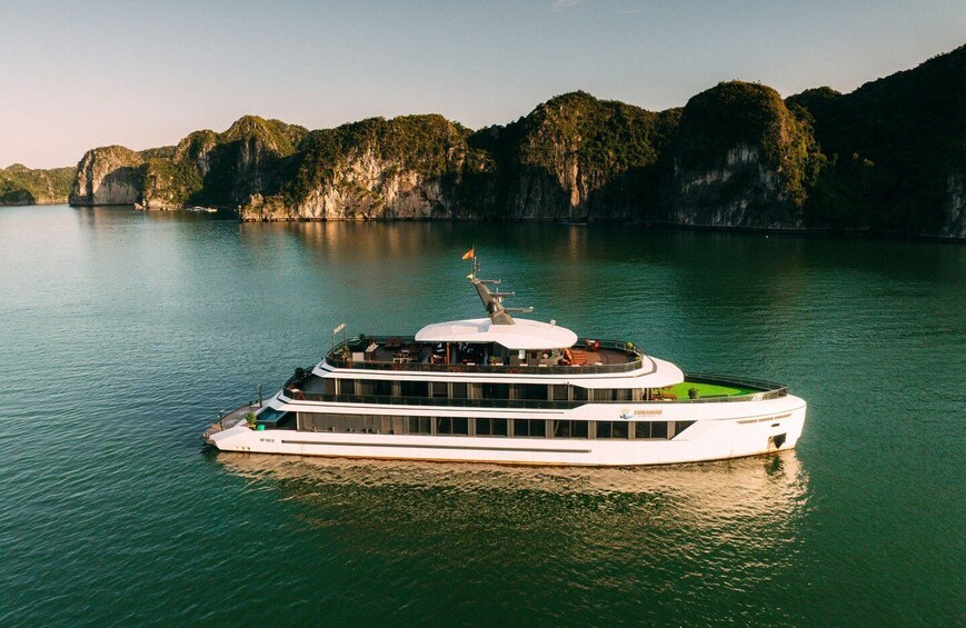 A white river cruise ship with multiple decks and a flag, floating on calm water with a mountainous coastline in the background. 4