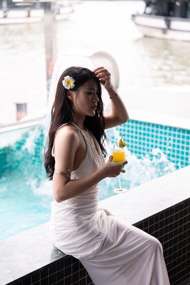 A person in a white dress sitting by a pool with a drink. 5