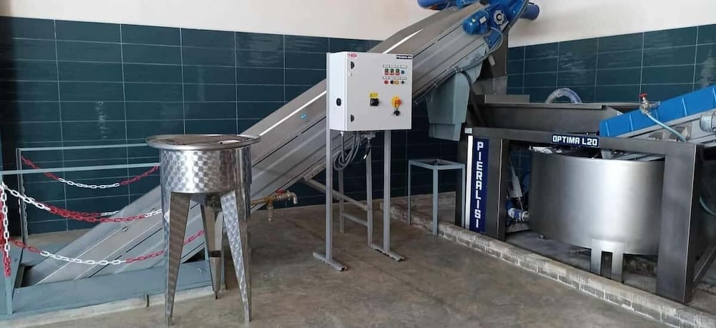 A conveyor belt system with a control panel, a metal stool, and a large stainless steel container. 5