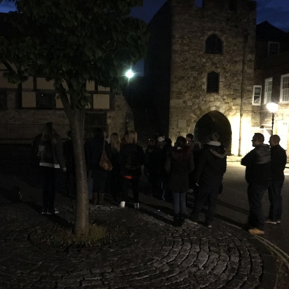 A group of people standing in front of a stone building with an arched entrance, illuminated by a street lamp. 3